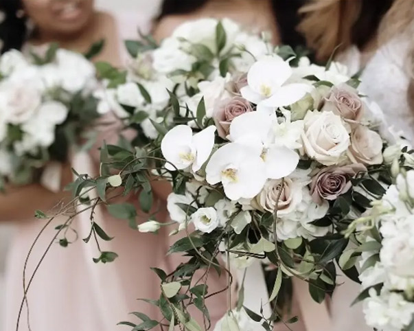 Bride holding cascading bouquet with white orchids, roses, and greenery.