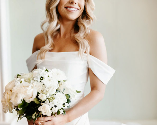 Bride with white and cream floral bouquet in an off-shoulder dress.